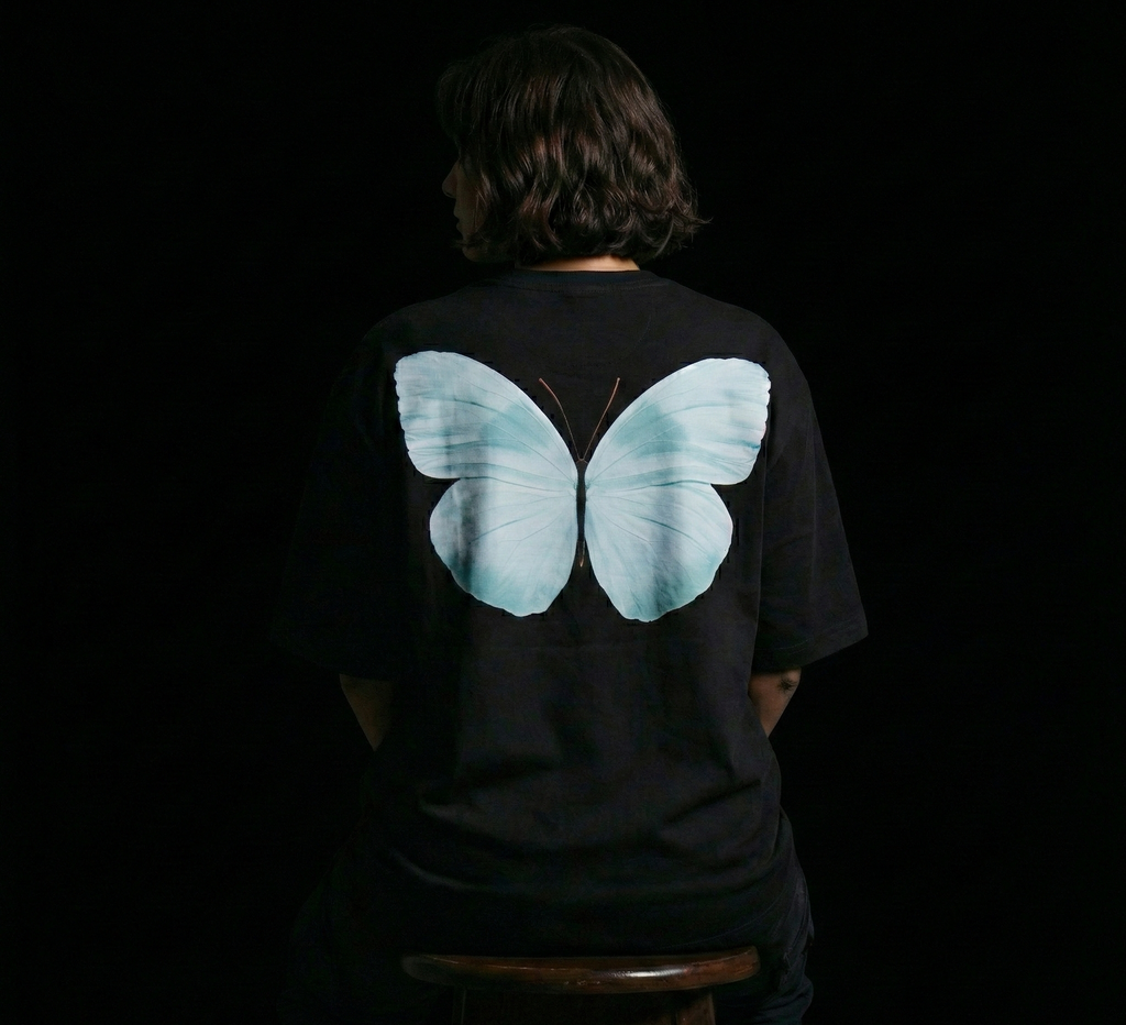 Person wearing a black t-shirt with a large blue butterfly design on the back against a dark background