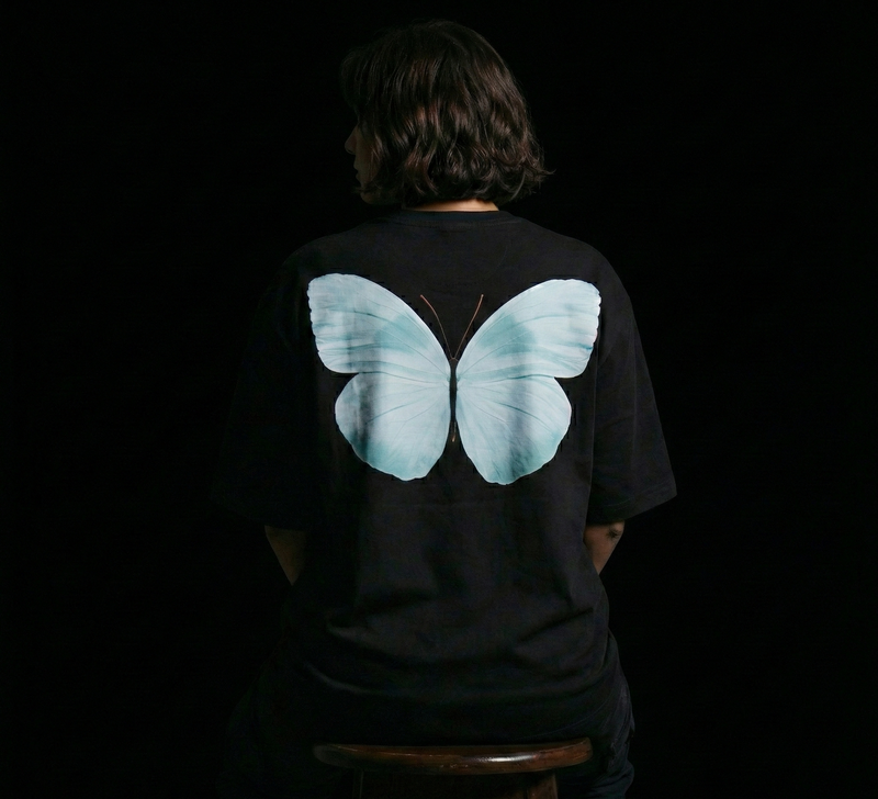 Person wearing a black t-shirt with a large blue butterfly design on the back against a dark background