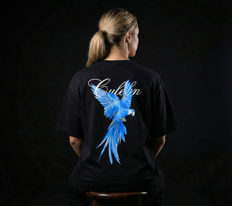 Person wearing a black t-shirt with a blue macaw design on the back against a dark background