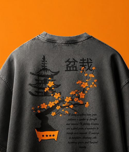 A dark gray washed graphic t-shirt shown from the back, featuring a black pagoda and Chinese characters with an orange cherry blossom tree design and English text, set against a solid orange background.