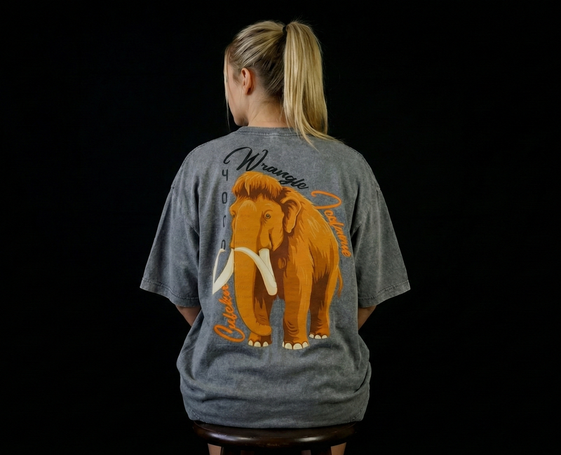Person wearing a gray t-shirt with a wooly mammoth graphic on the back against a black background